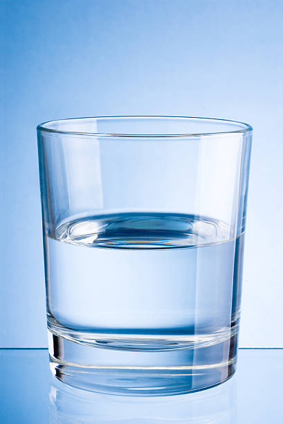 un demi-verre d'eau potable sur fond bleu - glass water half full empty photos et images de collection