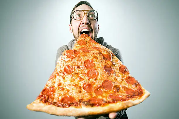 An excited adult man gets ready to take a bite out of a ridiculously large slice of pepperoni pizza, a look of excitement and joy on his face.  Horizontal image with copy space.