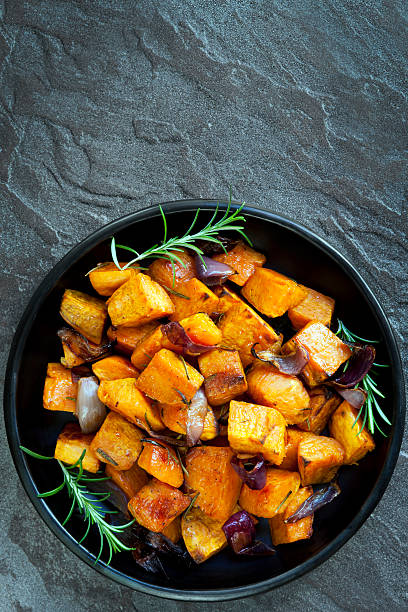 Roasted sweet potato with red onion and rosemary.  Black dish, overhead view, over dark slate.