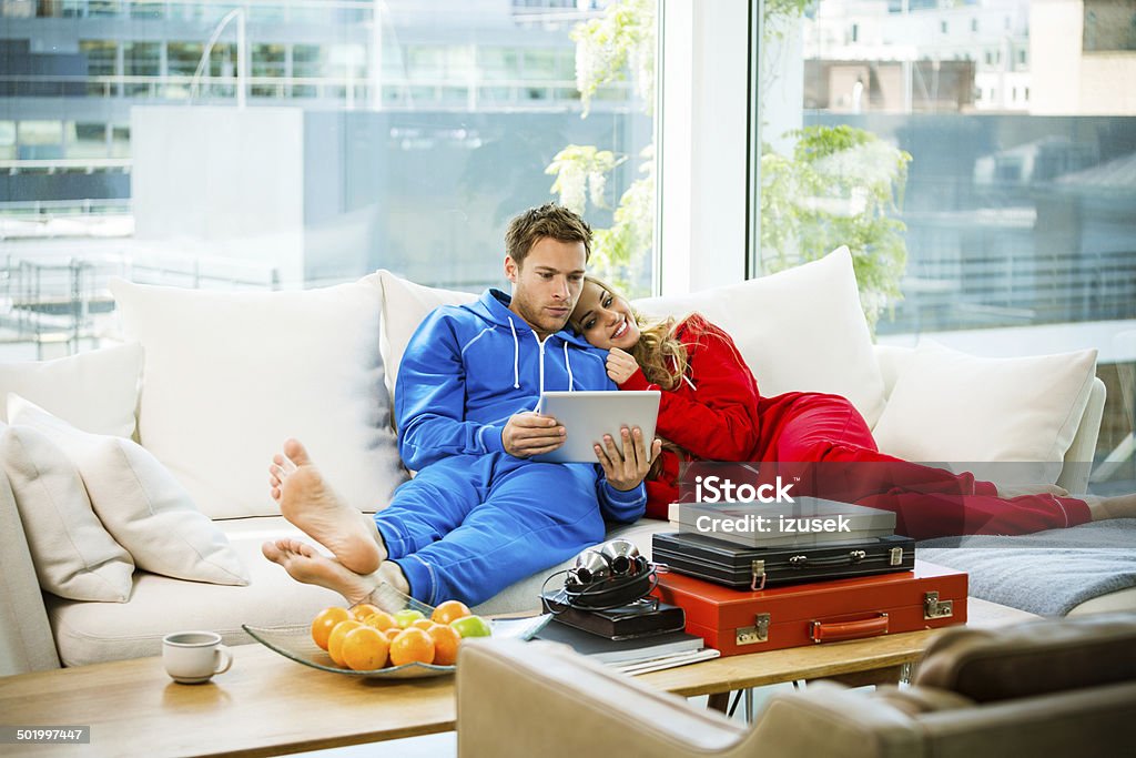 Young couple in an apartment Young couple lying down on sofa in their apartment and using a digital tablet together.  20-24 Years Stock Photo