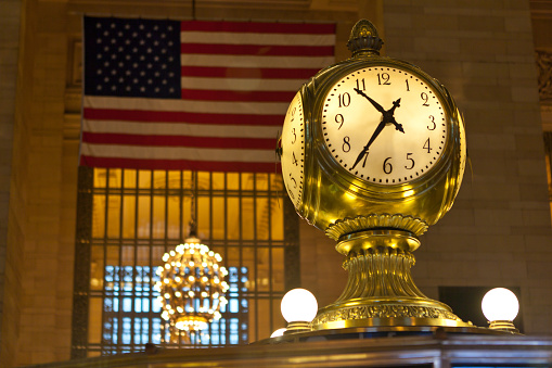 New York, USA - January 27, 2012: Clock at Grand Central Terminal with American flag in the background in New York, NY pon January 27, 2012. This four-faced clock on top of the information booth is the most recognizable icon of Grand Central Station. 