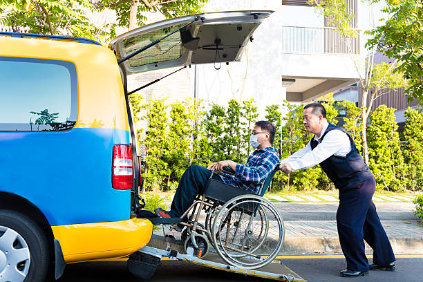 driver helping man on wheelchair getting into taxi stock photo