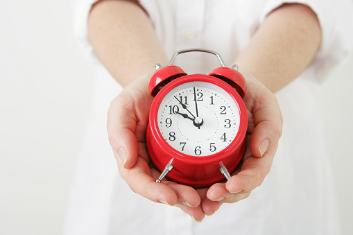 A woman's hands holding a red alarm clock.