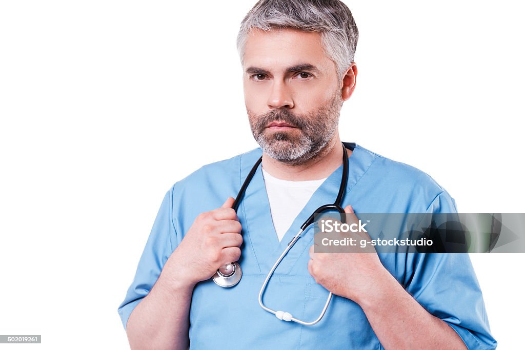 Confident surgeon. Confident mature doctor in blue uniform looking at camera and adjusting his stethoscope while standing isolated on white Active Seniors Stock Photo