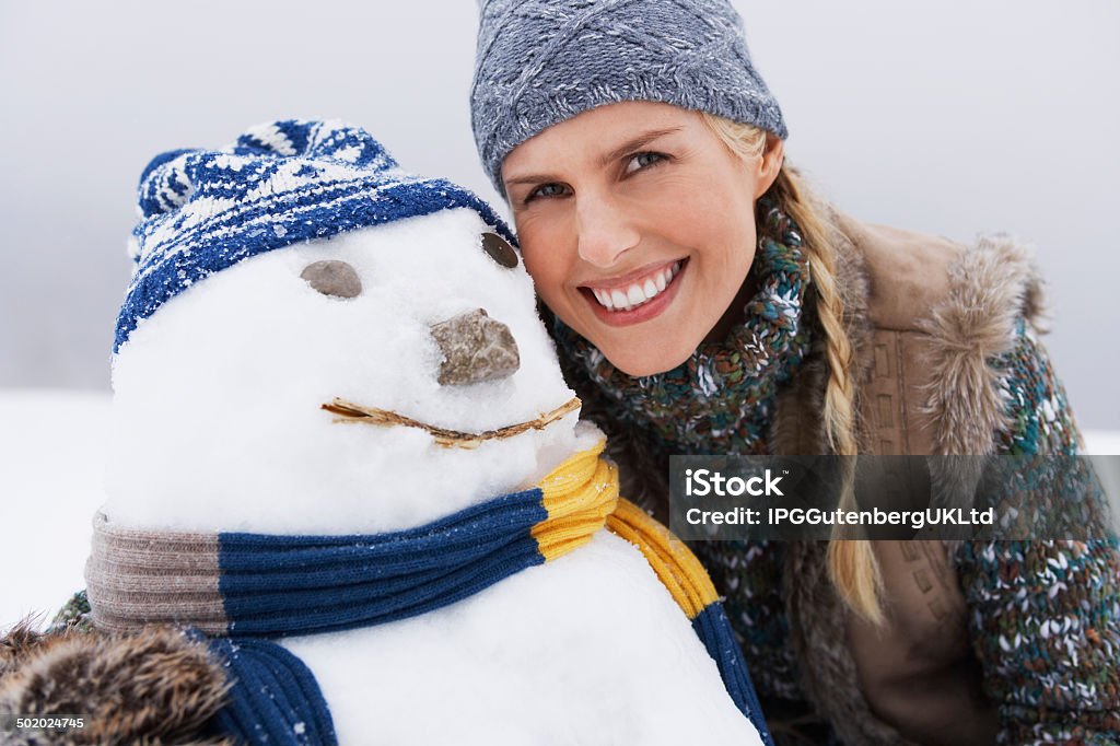 Cheerful Young Woman By Snowman Closeup of a cheerful young woman by snowman on snow covered hill Adult Stock Photo