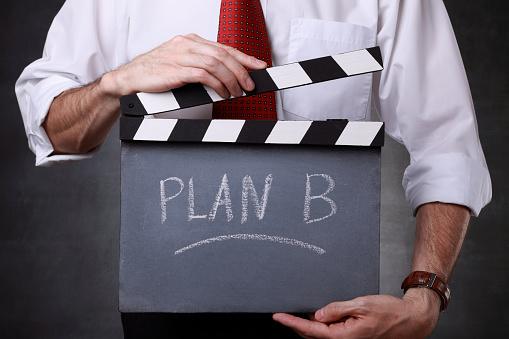 Businessman holding a clapper in front of blackboard. He's ready to start plan B.