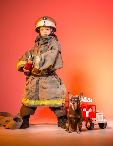 Little boy dressed as firefighter with a fire hose and a little dog on a red background