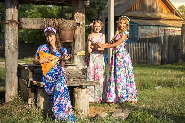 Three beautiful Russian girls making merry at the well on a summer evening in a countryside