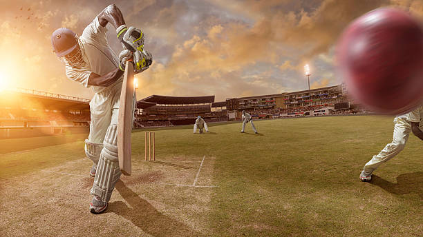 Cricket Action A close up mid action image of a professional cricket batsman having just hit ball during a cricket game. The action takes place in a generic floodlit outdoor cricket ground full of spectators under a cloudy summer sky at bright sunset.  Batsman and fielders are all wearing unbranded cricket whites.   cricket player stock pictures, royalty-free photos & images