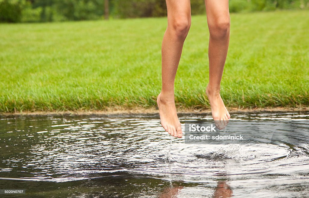 Child's Feet Jumping In Rain Puddle The feet and legs of a 12 year child jumping in a large puddle left after a storm. Barefoot Stock Photo