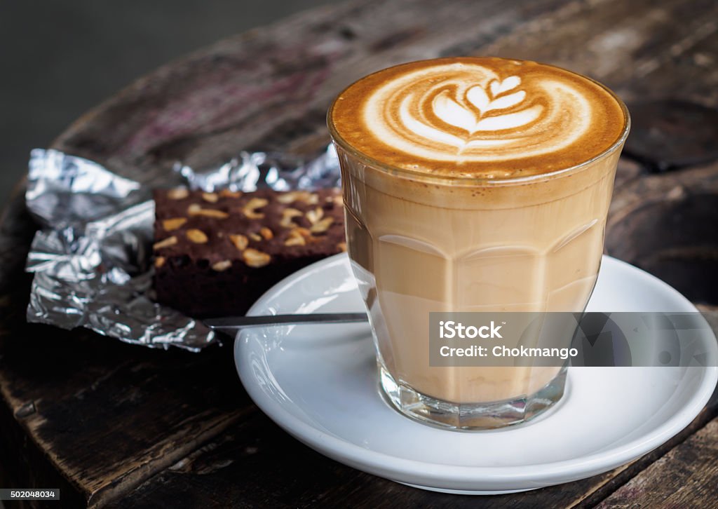 Hot latte coffee on old wooden table with brownie cake A cup of hot latte art or cappuccino coffee on old wooden table with brownie cake on foil Latte Stock Photo