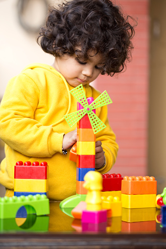 Little boy playing with colourful building blocks and making windmill on table, Early Childhood Development. Children like to think hard about what they are doing and try out their own ideas. They can solve the problem of building blocks so they will stand high.