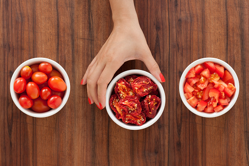 Three bowls with varieties of tomato and woman's hand holding the middle one