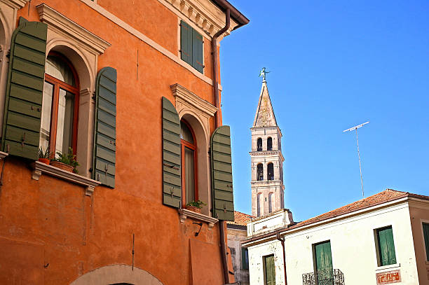 view of the wall of the house with windows and green shutters and the bell tower