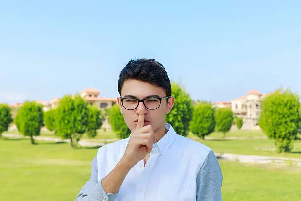 Serious young man placing finger on lips with shhh sign symbol.