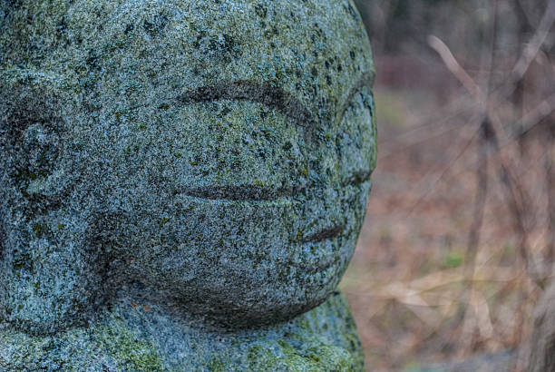 Stone Buddha Sculpture Close in Woods A full frame image of the face of a stone buddha sculpture in the woods.   The stone is old and weathered.   The forest floor behind the sculpture is out of focus.  Highly textured. peacful stock pictures, royalty-free photos & images