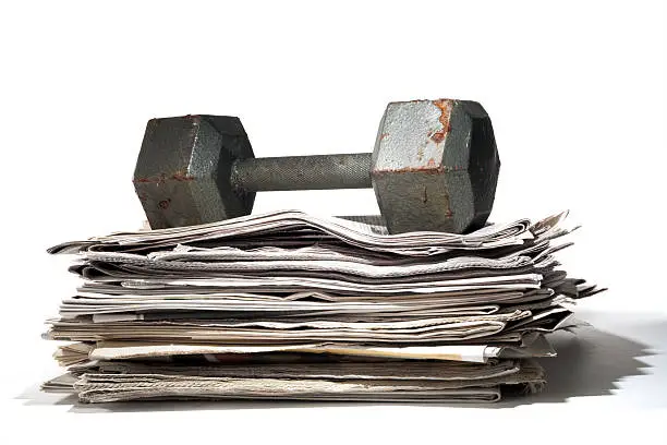 A stack of newspapers under a heavy dumbbell. The dumbbell is misused as it is rusted and employed as a paper weight.