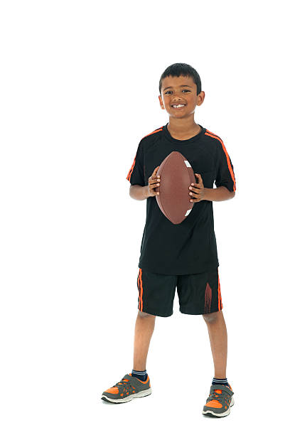 Dynamic image of young boy in mid-air, dressed in red soccer jersey and black shorts, skillfully heading soccer ball on white background. Concept of professional sport, championship, youth league. Ad