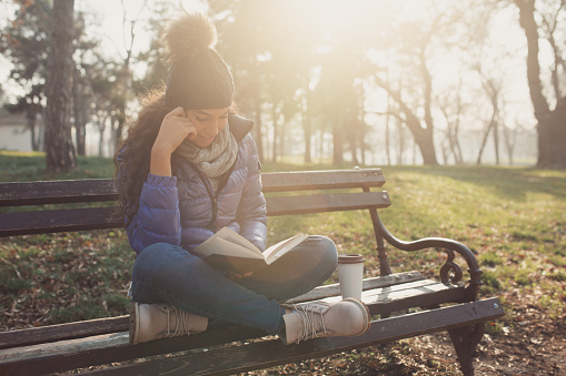 Girl sitting on the bench at the park and reading a book.