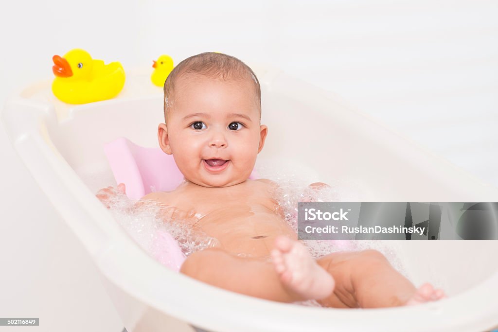 Baby enjoying bath. Adorable baby girl doing shower, lying on bath support and looking at camera. Baby Bathtub Stock Photo