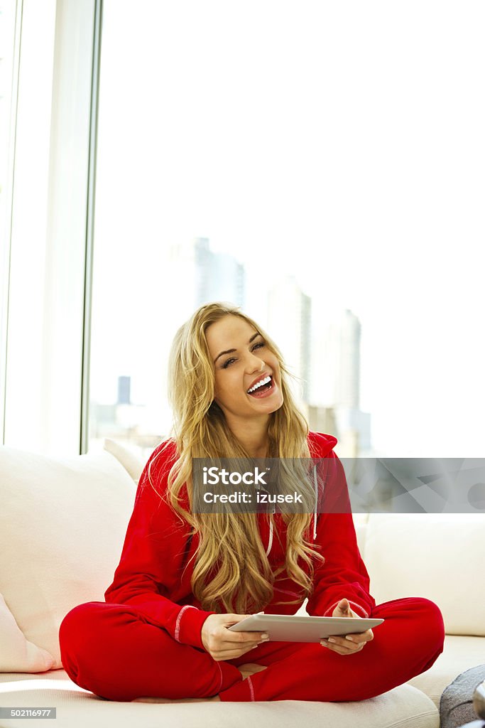 Young woman with digital tablet Young woman wearing overalls sitting on sofa at home in the morning, holding digital tablet in hands and smiling at camera. Bib Overalls Stock Photo