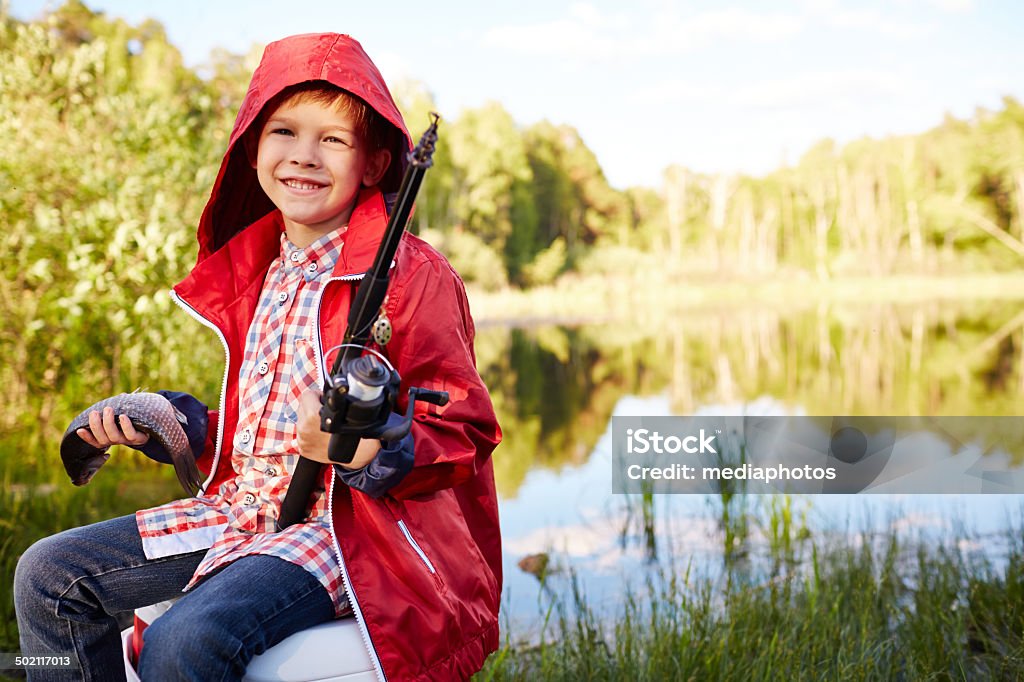 Happy fisher boy Cheerful kid sitting on riverbank with fishing rod and freshly-caught fish 2014 Stock Photo