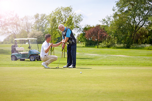 Golf pro teaching senior male golfer on putting green