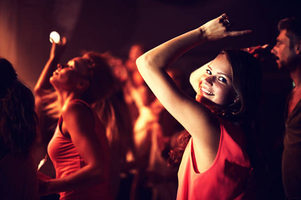 Shot of a young woman dancing with her arms in the air with people in the background. This concert was created for the sole purpose of this photo shoot, featuring 300 models and 3 live bands. All people in this shoot are model released.