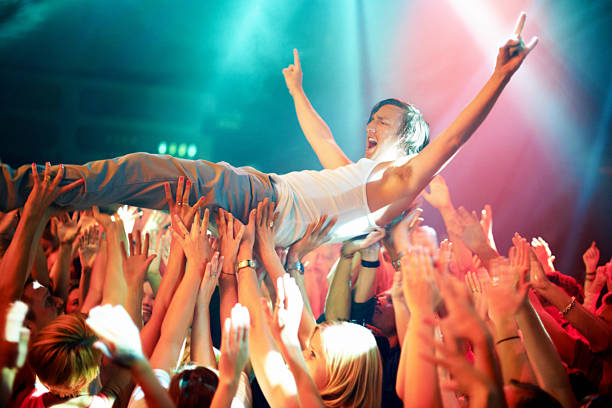 Riding a wave of fans A young man cheering as he crowd surfs at a concert. This concert was created for the sole purpose of this photo shoot, featuring 300 models and 3 live bands. All people in this shoot are model released. mosh pit stock pictures, royalty-free photos & images