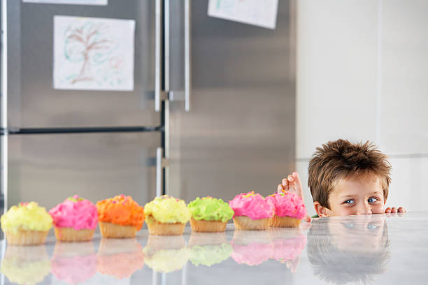 Boy Peaking Over Counter At Row Of Cupcakes Happy young boy peaking over counter at row of cupcakes in kitchen kid peaking over counter stock pictures, royalty-free photos & images