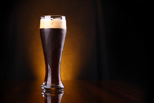 Tall glass of dark beer over a dark background lit yellow