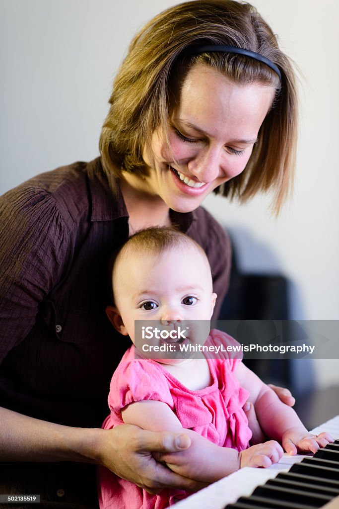 Excited Mother and Baby Playing Piano - Vertical A happy mother sitting at a piano with her baby girl.  2-5 Months Stock Photo