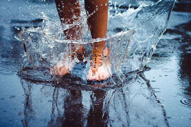 Jumping in the puddle Unrecognizable person (female) is splashing water in a puddle on a rainy day in the city. jumping into water stock pictures, royalty-free photos & images