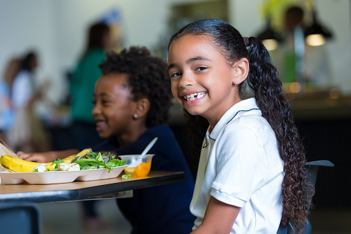 Cute elementary school girl eating healthy lunch in school cafeteria
