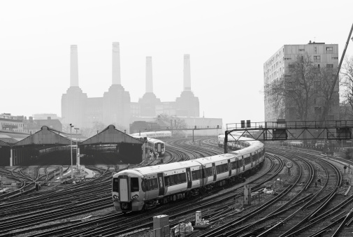 Moving local trains and railway tracks in London, with Battersea Power Station to be recognized behind the fog in the background. Black and White.