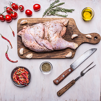 half raw chicken,Ingredients for cooking, tomatoes, knife and fork for the meat, peppers on wooden rustic background top view