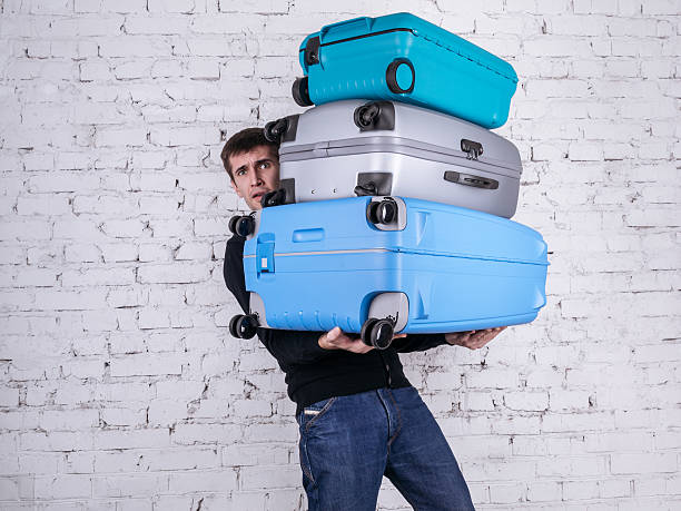 The man with the suitcases Unhappy man holding three heavy suitcases in hand. Travel light. excess stock pictures, royalty-free photos & images