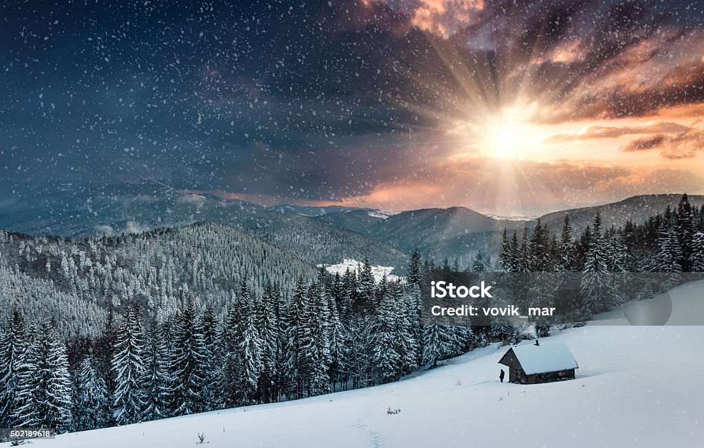 Winter mountains. View of  farm and tourist near. Colorful winter evening in the mountains at sunset. Dramatic overcast sky and snowing. View of the old farm and tourist near. Log Cabin Stock Photo