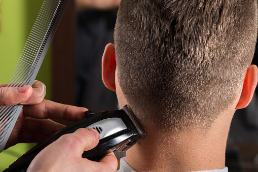 Hairdresser cutting clients hair with an electric hair clipper at beauty salon