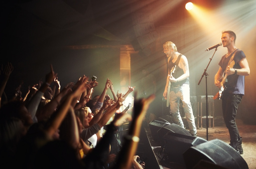 Shot of a crowd of music fans reaching up at a guitarist on stage. This concert was created for the sole purpose of this photo shoot, featuring 300 models and 3 live bands. All people in this shoot are model released.