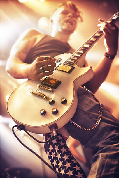 Rock out! Low angle view of a guitarist playing at a gig. This concert was created for the sole purpose of this photo shoot, featuring 300 models and 3 live bands. All people in this shoot are model released. bass instrument stock pictures, royalty-free photos & images
