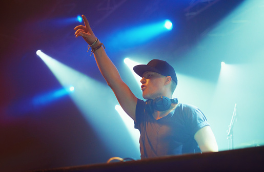 A DJ playing music on stage and engaging with the crowd. This concert was created for the sole purpose of this photo shoot, featuring 300 models and 3 live bands. All people in this shoot are model released.