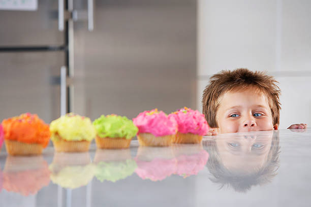 Boy Peaking Over Counter At Row Of Cupcakes Happy young boy peaking over counter at row of cupcakes in kitchen kid peaking over counter stock pictures, royalty-free photos & images