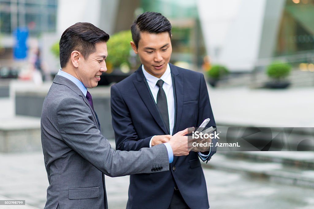 Coffee break Two asian businessmen talking outdoors and looking at mobile phone. 25-29 Years Stock Photo