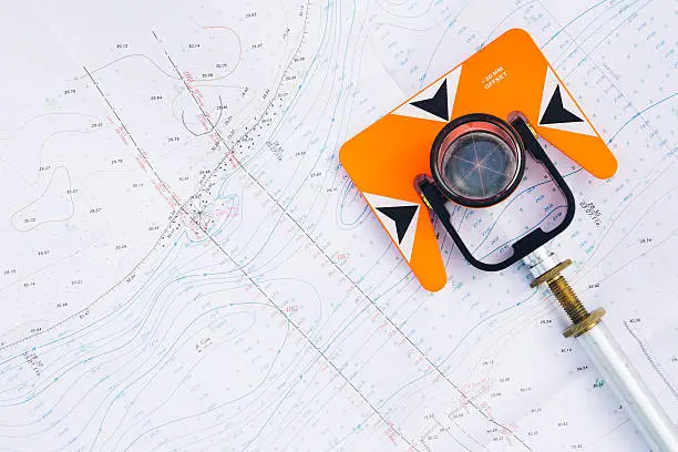 Photo of orange theodolite prism lies on a background geodetic maps