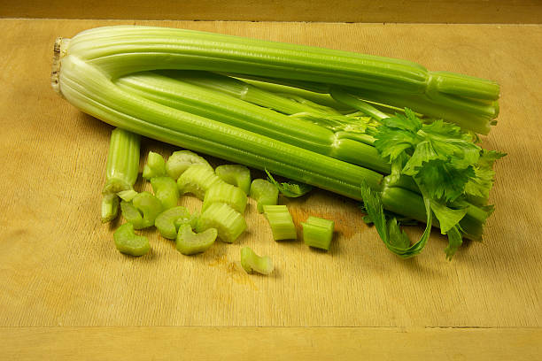 Bunch of fresh,green celery and cut into pieces one stalk at an old, wooden pastry board kitchen. Horizontal view.