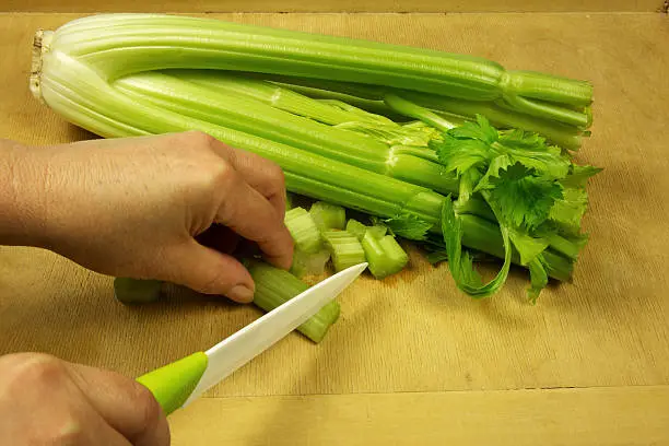 Housewife with a knife cuts fresh celery on an old wooden pastry board. Close,horizontal view.