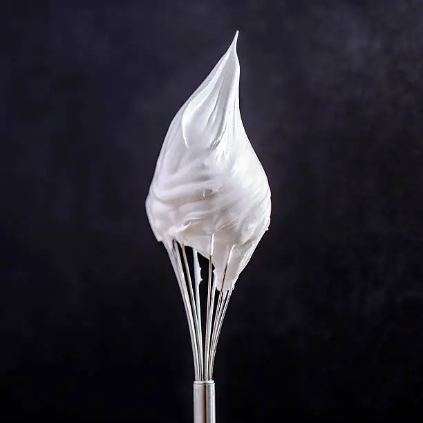 whip cream on top of whisk on black background