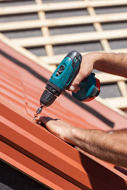 istock Worker on roof with electric drill installing red metal tile 502216510