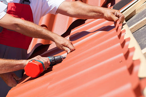 Workers on roof with electric drill installing red metal tile